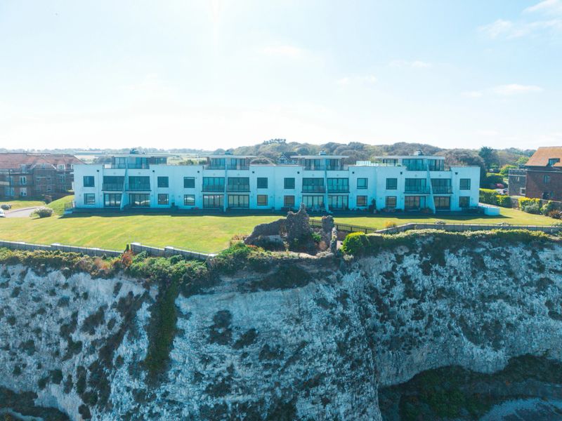 White modern apartments with balconies sitting on a green lawn overlooking white chalk cliffs