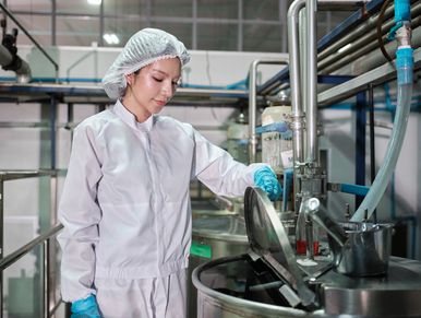 A technician in protective clothing operates industrial machinery in a clean factory environment.