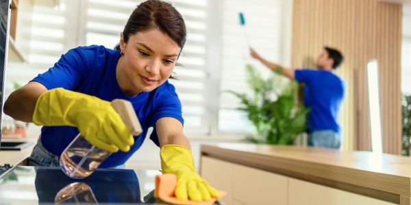 Woman cleaning kitchen surface wearing yellow gloves.