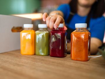 A person picking up a red juice bottle among various colorful juice bottles.