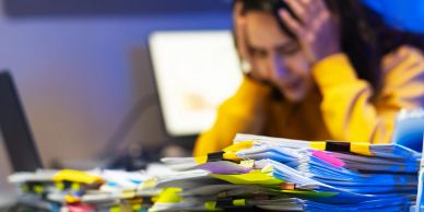 A person overwhelmed by a large stack of documents.