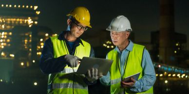 Two workers in safety gear reviewing documents at night.