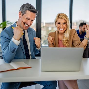 Two colleagues celebrating success in front of a laptop.
