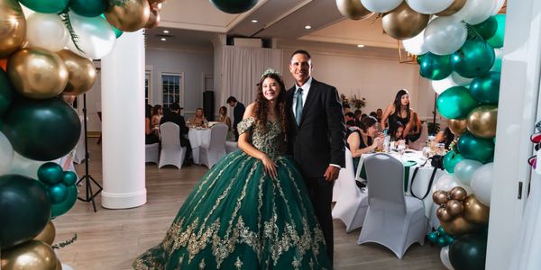 Young woman in a green ball gown with a man at a decorated indoor event.