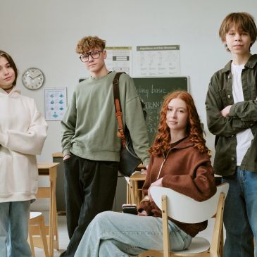 Group of four teenagers posing confidently in a classroom.
