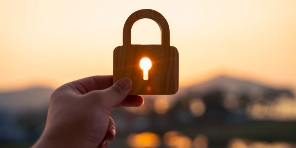 Hand holding wooden lock with sunlight shining through keyhole.
