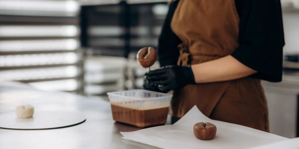 Person dipping doughnut in chocolate glaze.