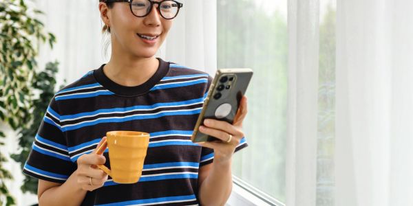 Smiling woman holding a cup and looking at her phone.