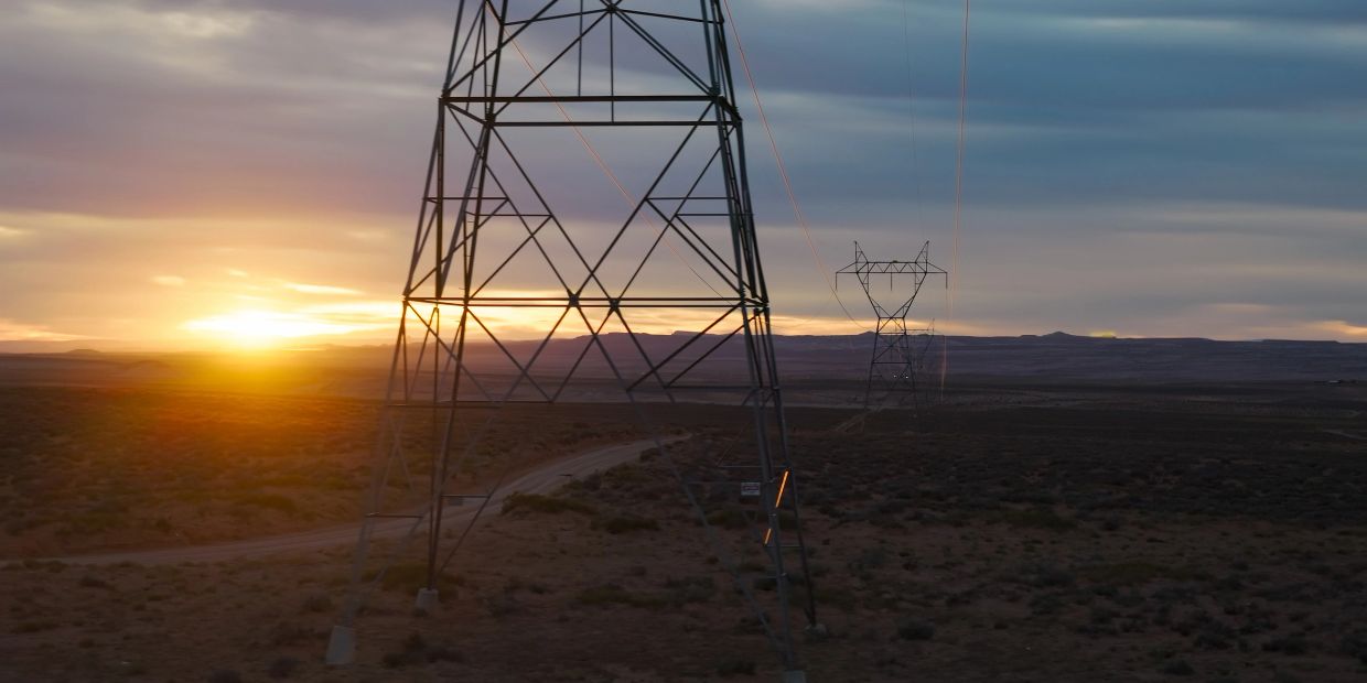 Sunset behind power transmission towers in a vast desert landscape.