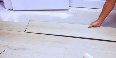 Person installing wooden laminate flooring near a white door.