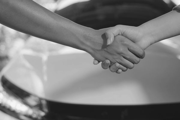 Two people shaking hands in front of a car.