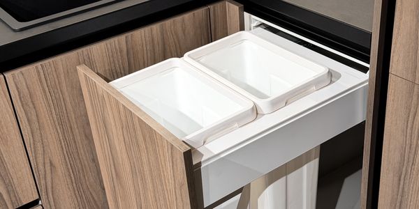 Pull-out drawer with two white bins in a wooden kitchen cabinet.