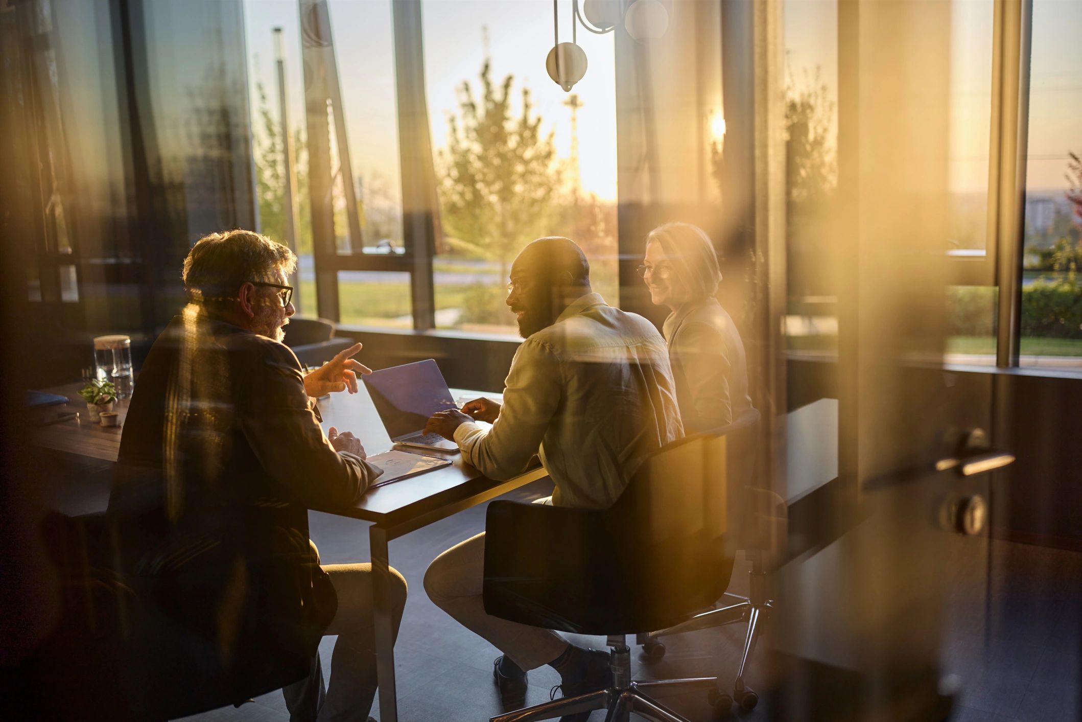 Tres personas discutiendo en una sala iluminada por el sol.
