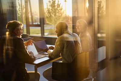Three people discuss work in a sunlit office.