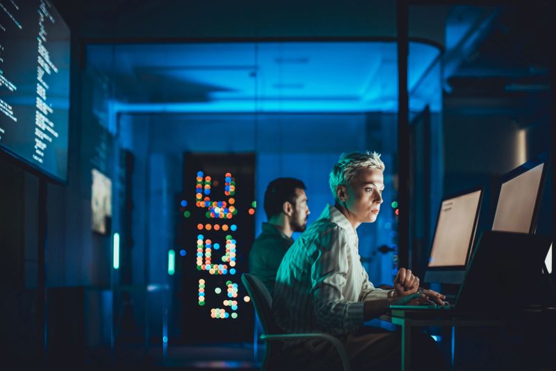 Short haired woman working at computer in modern data center with male colleague nearby