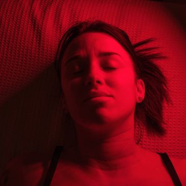 Woman lying down with red lighting and closed eyes.