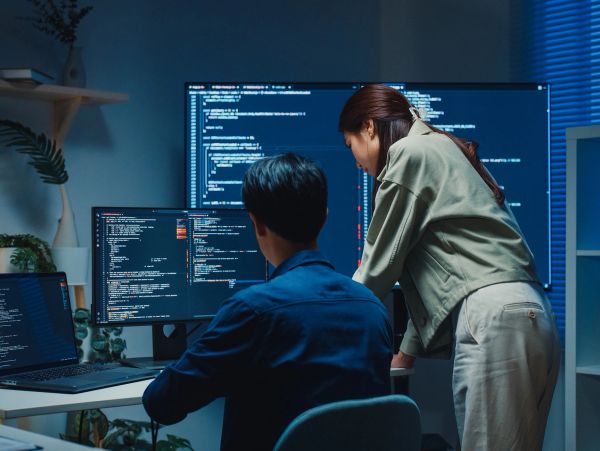 Two people collaborating on coding at multiple screens.