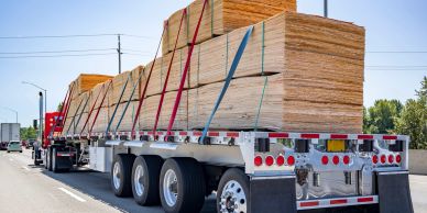 A truck carrying a large load of lumber secured with straps.
