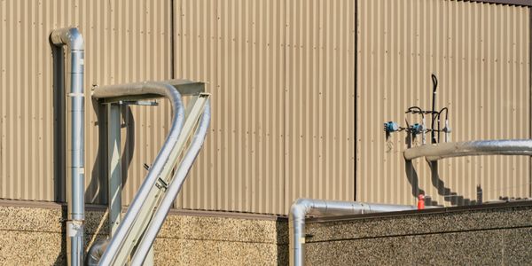 Industrial pipes and valves attached to a beige corrugated metal wall.