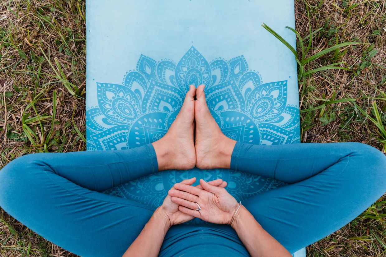 Person sitting cross-legged on a yoga mat outdoors.