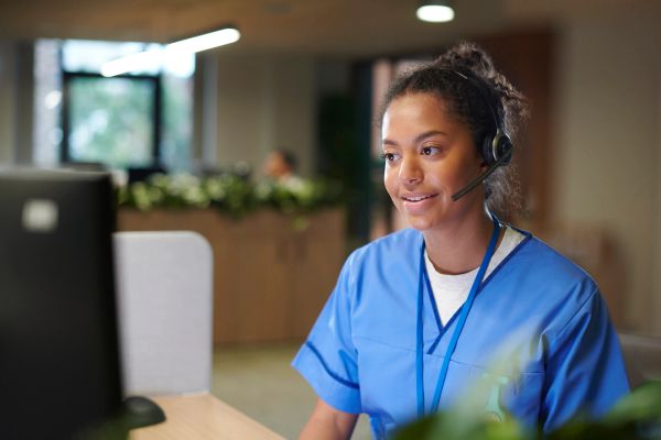 Healthcare worker with headset smiling at computer.