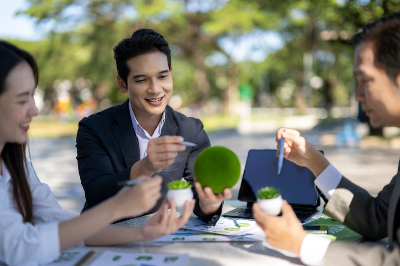 Business professionals collaborating on an eco-friendly project while holding green items at an outdoor meeting