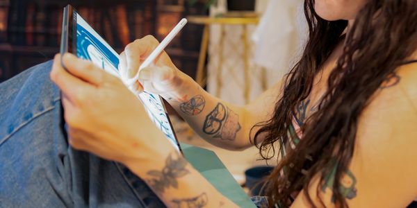Person drawing on a tablet with a stylus, showing tattooed arms.