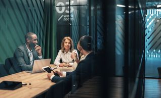 Three professionals in a meeting room having a discussion.