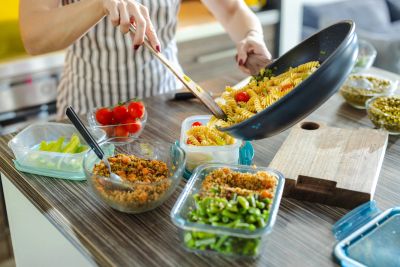 Person preparing pasta meal in containers.