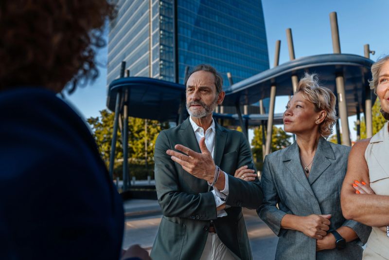 Group of diverse business professionals having a serious discussion outdoors, with a modern city building in the background