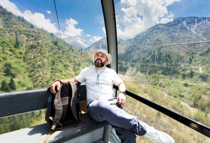 Mid adult man travelling in mountains at summer, going up funicular and enjoying the view