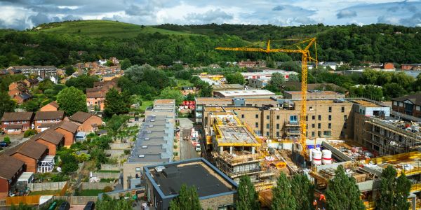 Construction site near a residential area with greenery and hills.