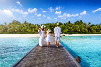Family walking on a pier toward a tropical beach.