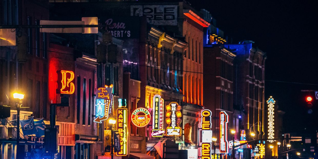 Colorful neon signs light up a downtown street at night.