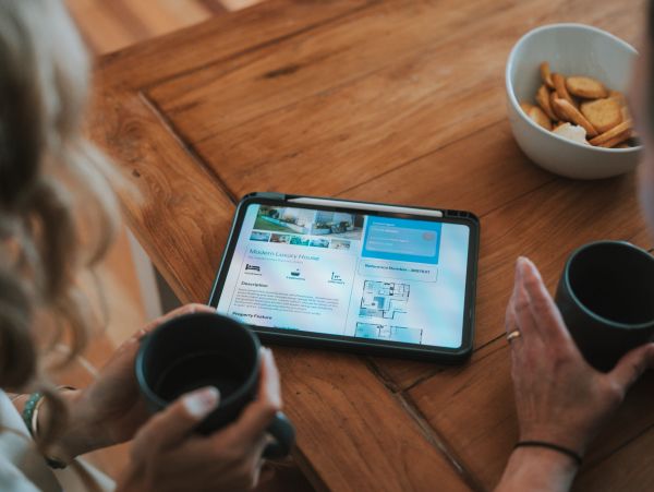 Two people browsing a real estate listing on a tablet over coffee.