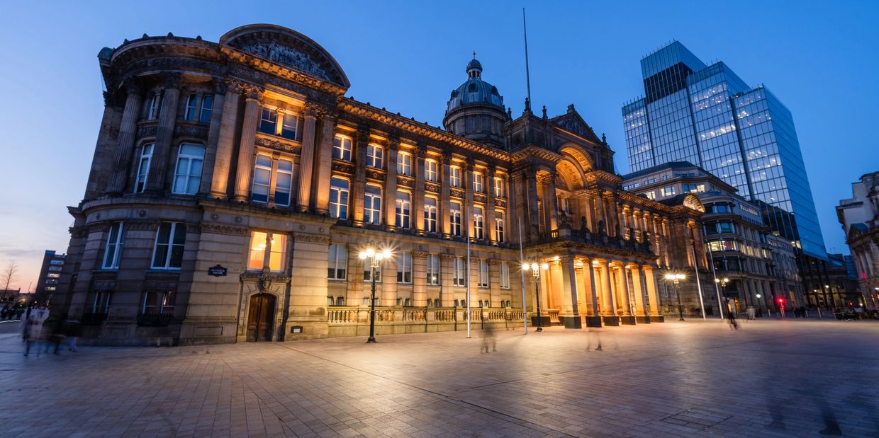 Grand historic building illuminated at dusk in a city square.