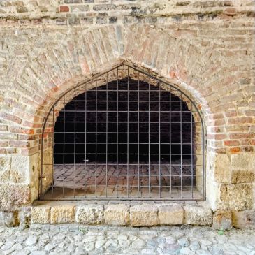 Arched brick window with metal grid in an old stone wall.