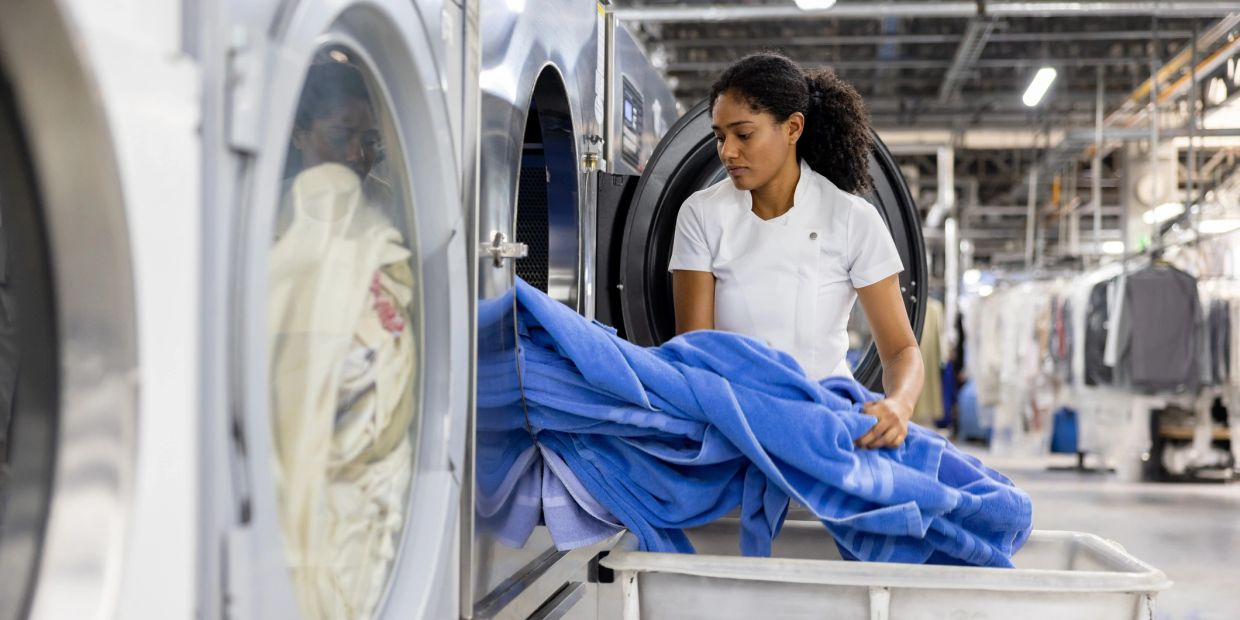 Woman loading blue laundry into industrial washing machine.