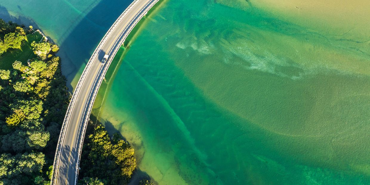 Aerial view of a curved bridge over clear turquoise water and green trees.