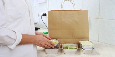 Person packing takeout containers into a paper bag.