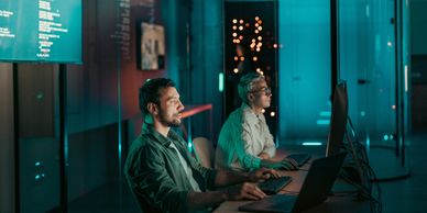 Two programmers working late in an office with code on screens.