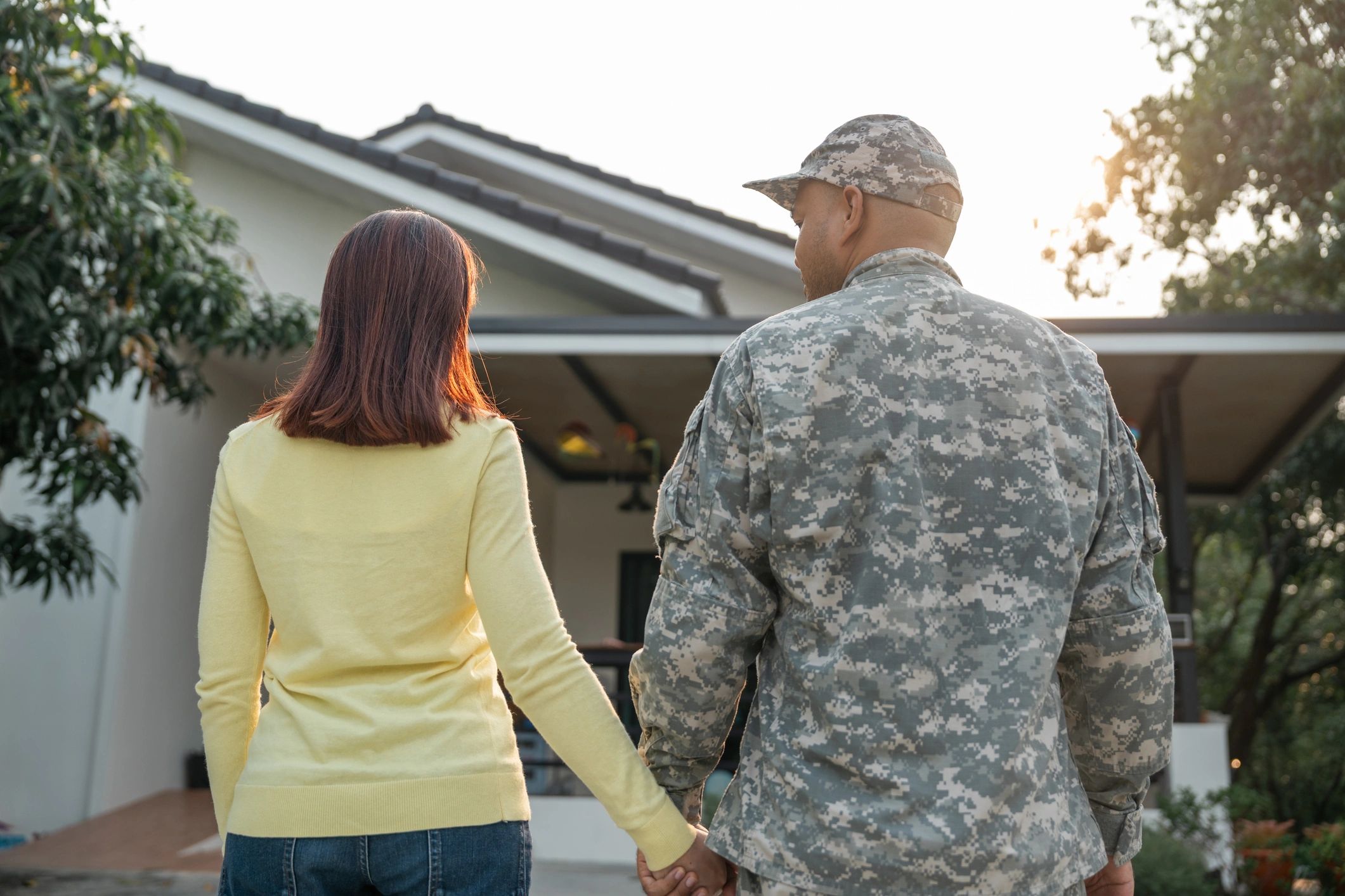 Couple holding hands outside a house, one in military uniform.