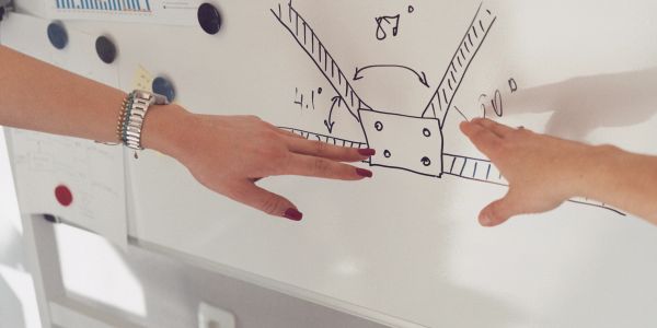 Two hands pointing at a diagram on a whiteboard.