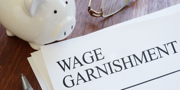 Documents titled Wage Garnishment with piggy bank and glasses nearby.