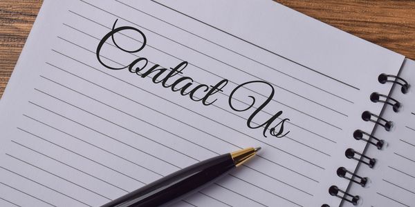 Spiral notebook with 'Contact Us' written and a pen.