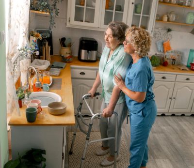 Senior woman with walker receiving in-home care assistance from a caregiver in her kitchen"