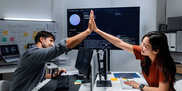 Two coworkers high-five over a successful project at their desks.