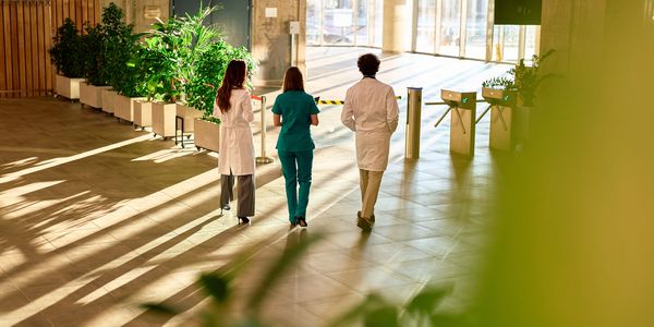Three medical professionals walking in a sunlit hallway.