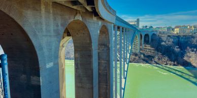 A large concrete arch bridge over a green river.