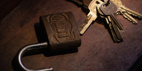Old open lock and keys on wooden surface.